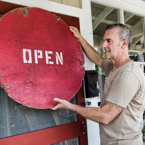 A middle-aged man hangs an "Open" sign on the door of a shop