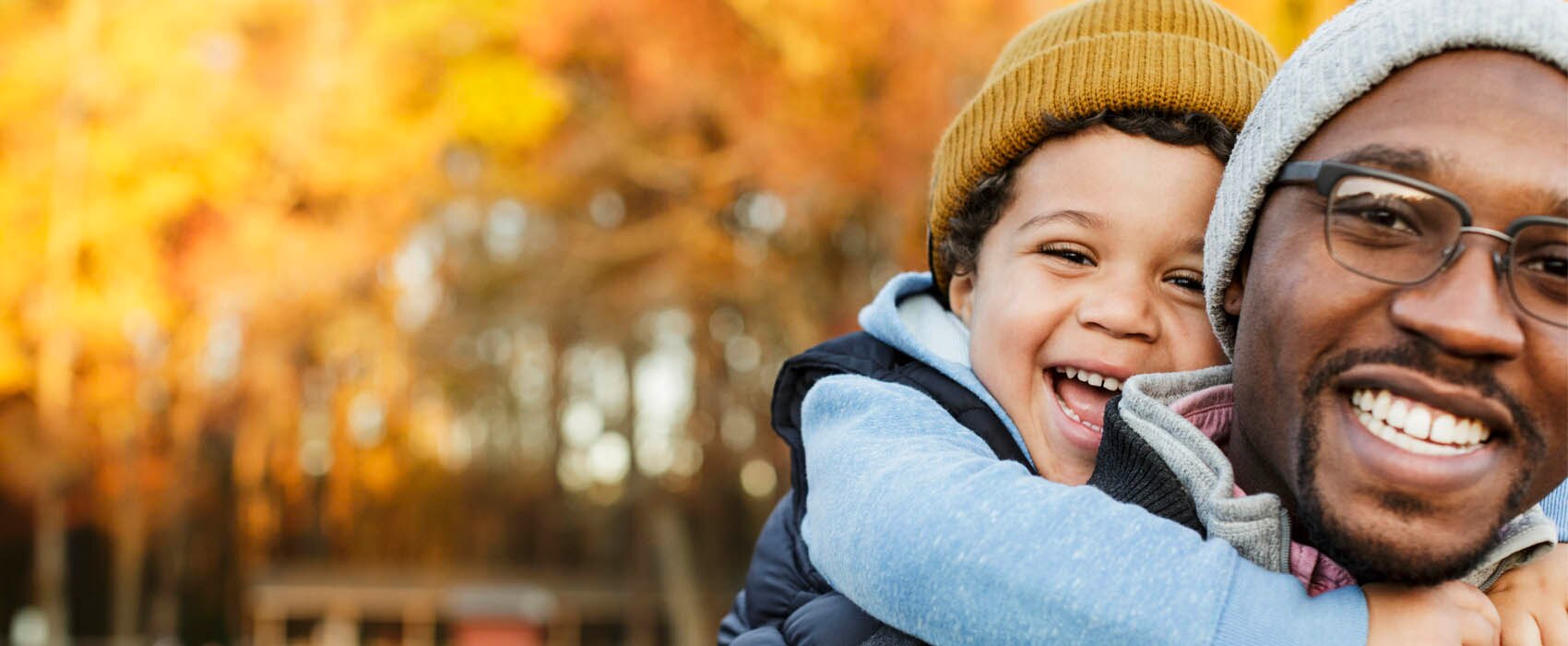 A man carrying his son on his back outdoors in autumn