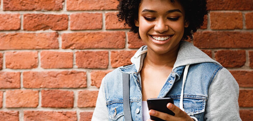 Woman smiling at phone in front of wall
