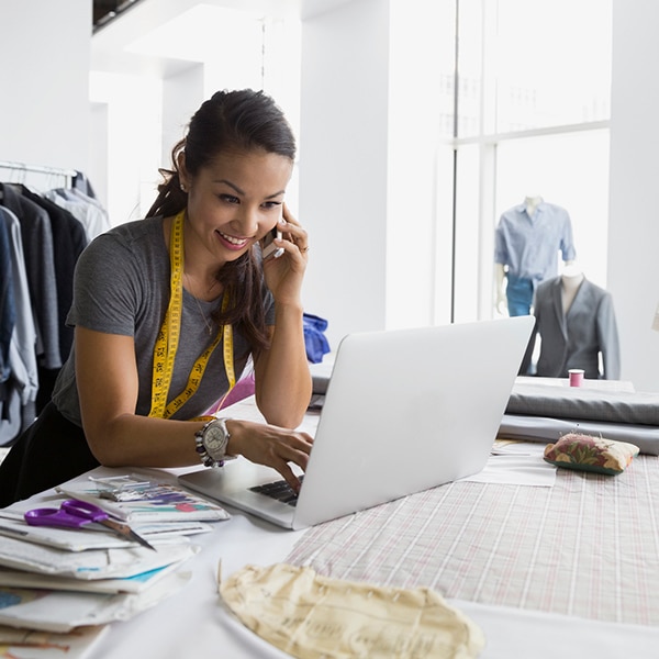 Fashion designer talking on her mobile phone while typing on her laptop