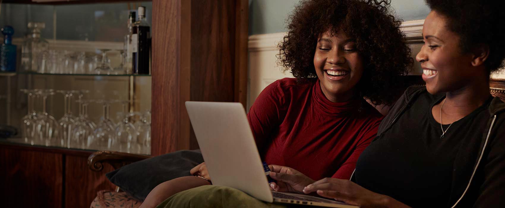 two smiling women sitting on couch using a laptop