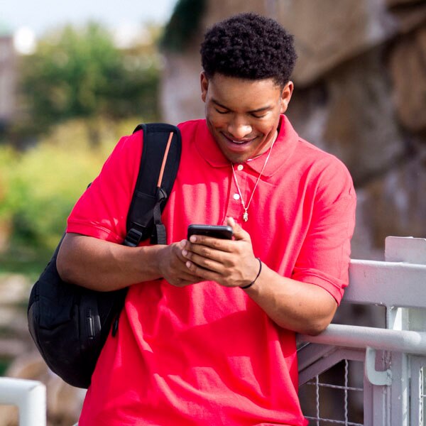 Boy leaning on a fence texting.