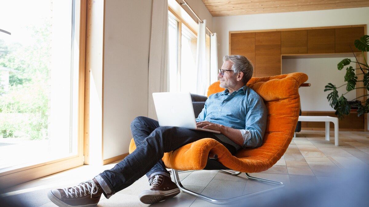 a man sitting in a chair working on his computer while staring out his window