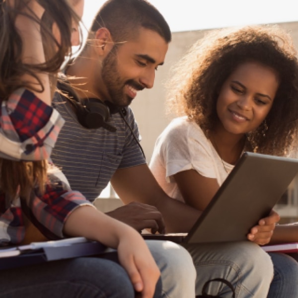 Students sitting together outside, looking at a laptop.