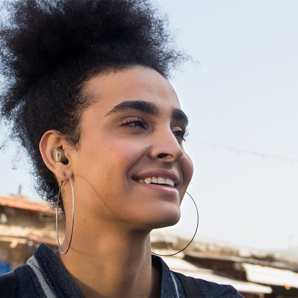 Person outdoors wearing earbuds and hoop earrings, with buildings visible in the background.