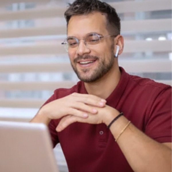 Man in maroon shirt attending virtual meeting on laptop