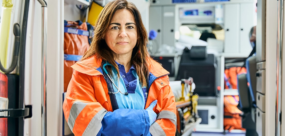 Healthcare worker standing inside an emergency vehicle wearing protective outerwear and a stethoscope.