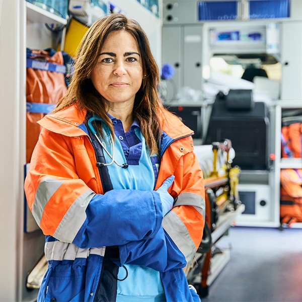 Healthcare worker standing inside an emergency vehicle wearing protective outerwear and a stethoscope.