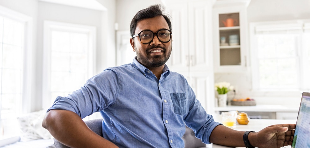 Person seated indoors in a kitchen or dining area, leaning back in a chair near a table.