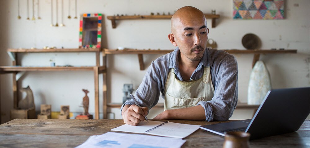 Shopkeeper at table with laptop and notebook