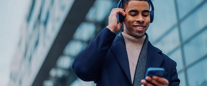 Well dressed man walking down street listening to a podcast via headphones