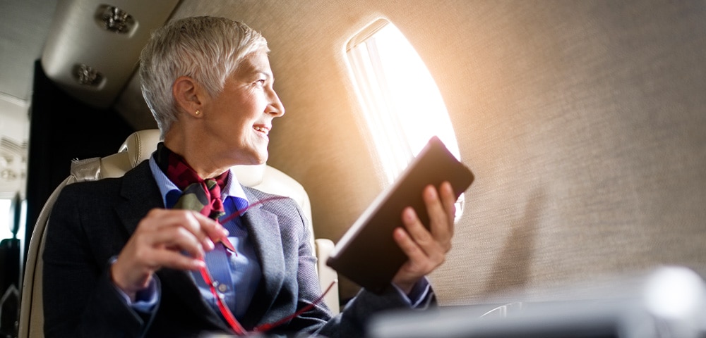 Woman looking out window of plane holding tablet.